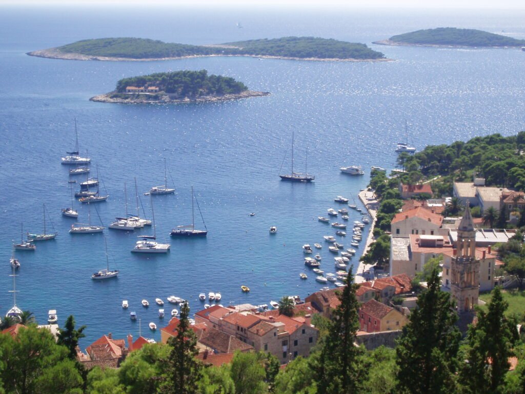 Voiliers sur la mer bleue, maisons aux toits de tuiles du port de Hvar et îles Pakleni à l’arrière-plan.