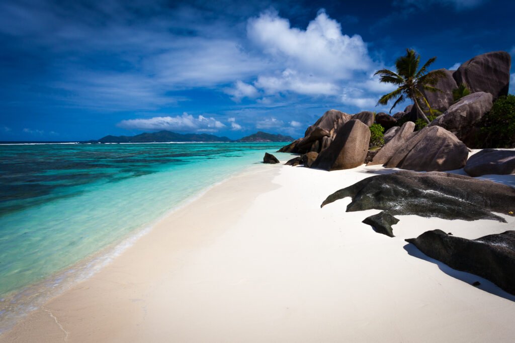 Sable blanc éclairé par le soleil, eau turquoise et rochers de granite bordés de palmiers à Anse Source d’Argent.